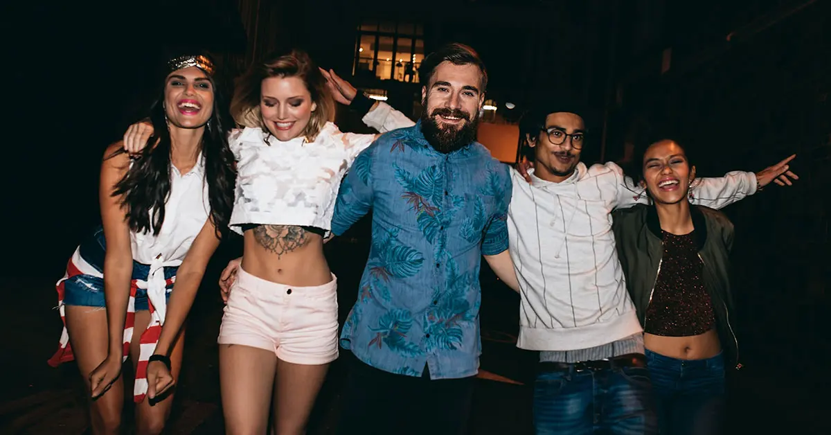 Grupo de amigos jóvenes sonriendo y abrazados durante una caminata nocturna por la ciudad.