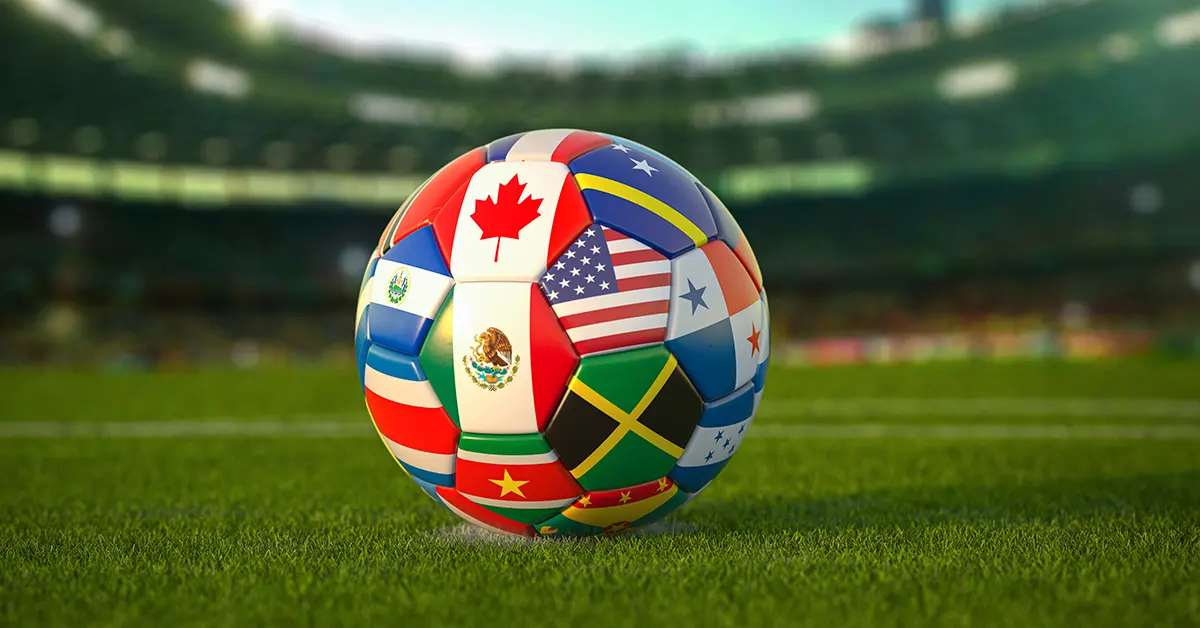 Balón de fútbol con patrones de banderas de diferentes países sobre el césped de un estadio profesional.